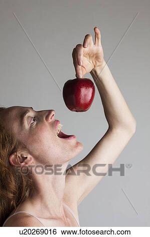 Stock Photograph - MODEL RELEASED. Profile of woman holding red apple above her head with mouth open.. Fotosearch