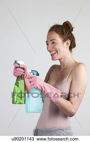 Stock Image - MODEL RELEASED. Smiling woman with protective gloves holding cleaning materials.. Fotosearch
