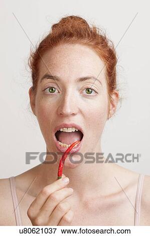 Stock Photo - MODEL RELEASED. Woman holding red chili pepper in front of her open mouth.. Fotosearch
