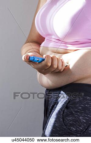 Stock Image - MODEL RELEASED. Woman injecting herself in the abdomen.. Fotosearch