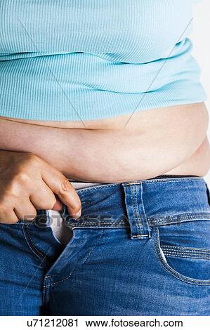 Stock Image - MODEL RELEASED. Woman trying to do up her jeans.. Fotosearch