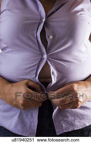 Stock Image - MODEL RELEASED. Woman trying to do up her shirt.. Fotosearch