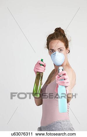 Stock Image - MODEL RELEASED. Woman wearing face mask and gloves holding cleaning materials in her hands.. Fotosearch