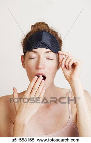 Stock Photography - MODEL RELEASED. Young tired woman yawning from lack of sleep wearing a sleeping mask.. Fotosearch