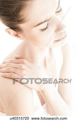 Stock Image - MODEL RELEASED. Young woman in pain rubbing her shoulder.. Fotosearch