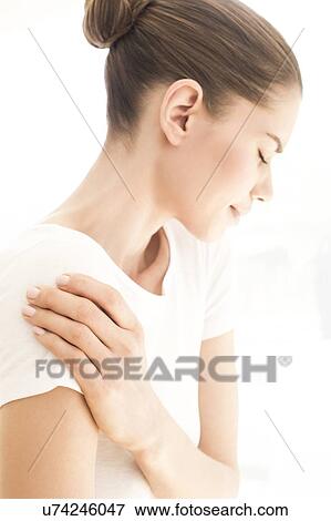 Stock Photo - MODEL RELEASED. Young woman in pain rubbing her shoulder.. Fotosearch