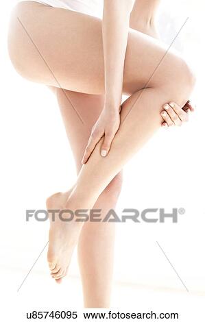 Stock Photography - MODEL RELEASED. Young woman in pain rubbing her leg, side view.. Fotosearch