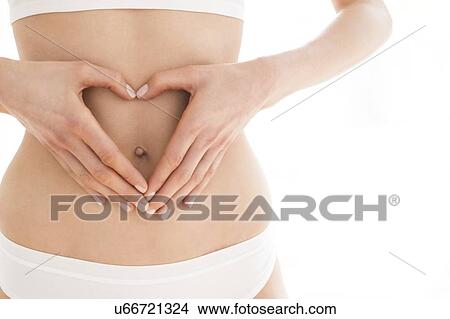 Picture - MODEL RELEASED. Young woman with hands in heart shape on tummy.. Fotosearch