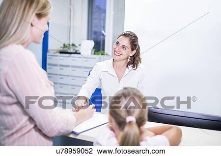 Stock Image - Mother and daughter talking to medical receptionist.. Fotosearch