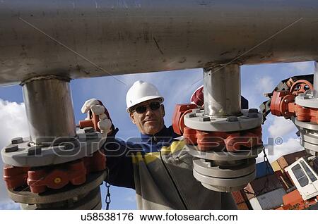 Stock Photograph - Oil and gas refinery worker turning on large pipelines.. Fotosearch