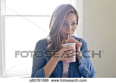 Stock Photograph - Portrait of young woman drinking through straw.. Fotosearch