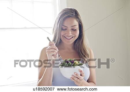 Stock Photo - Portrait of young woman eating salad.. Fotosearch