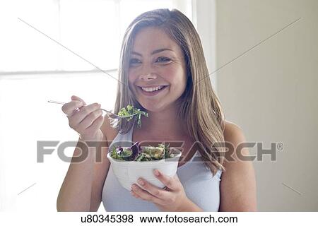 Stock Photo - Portrait of young woman eating salad.. Fotosearch