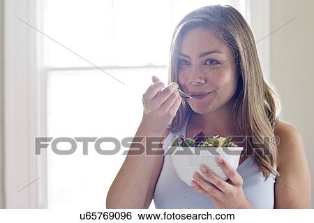 Stock Photograph - Portrait of young woman eating salad.. Fotosearch