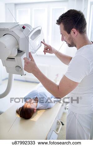 Stock Image - Radiologist positioning x-ray machine over female patient.. Fotosearch