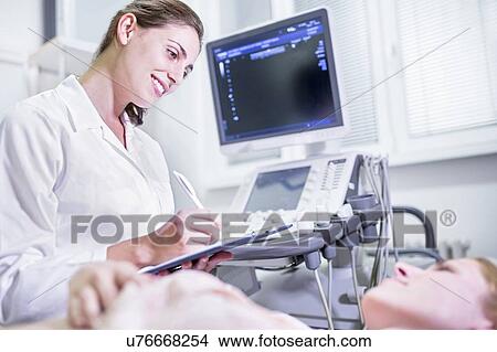 Picture - Sonographer making notes with female patient.. Fotosearch