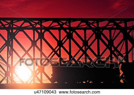 Stock Image - Train crossing bridge at sunset. Fotosearch