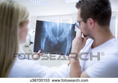 Stock Image - Two doctors holding x-ray of a male human pelvis.. Fotosearch