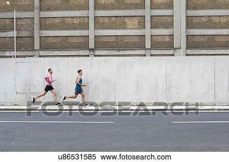 Stock Photography - Two men running on pavement next to concrete wall.. Fotosearch