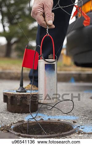 Stock Photograph - Water department technician lowering leak sensor.. Fotosearch