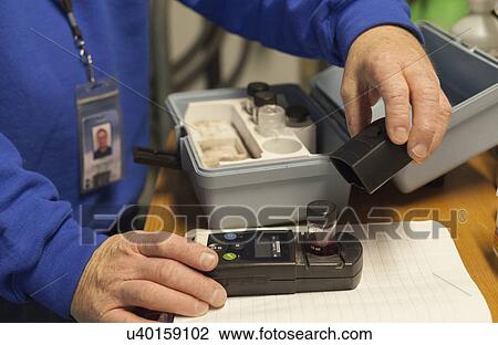 Stock Image - Water treatment engineer using hand held instrument on sample.. Fotosearch