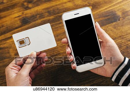 Stock Image - Woman holding smartphone and new SIM card. Fotosearch