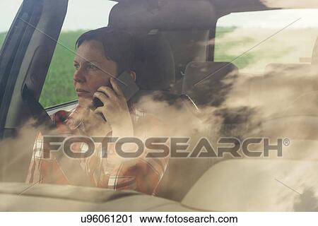 Stock Image - Worried woman talking on mobile phone in car. Fotosearch