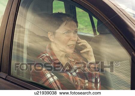Stock Photo - Worried woman talking on mobile phone in car. Fotosearch