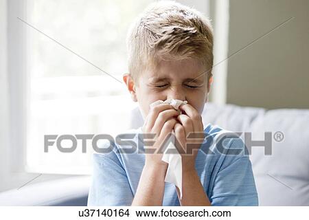 Picture - Young boy blowing his nose on a tissue.. Fotosearch