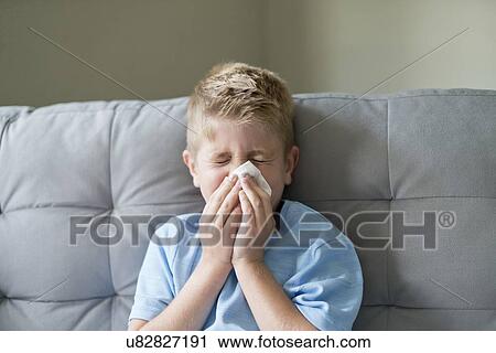 Stock Image - Young boy blowing his nose on a tissue.. Fotosearch