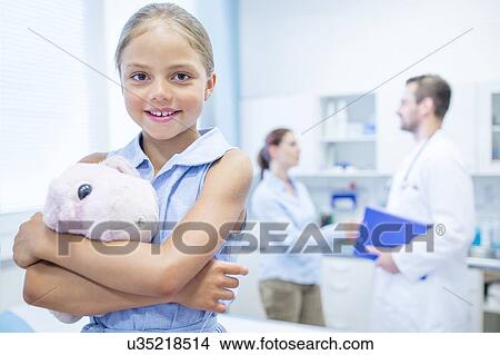 Young girl in doctor's room hugging teddy, smiling. View Large Photo Image Picture - Young girl in doctor's room hugging teddy, smiling.. Fotosearch