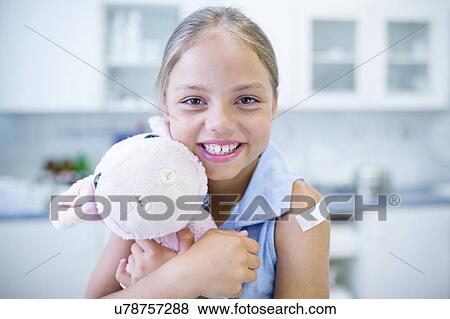 Young girl with plaster on arm hugging teddy after vaccination. View Large Photo Image Stock Photo - Young girl with plaster on arm hugging teddy after vaccination.. Fotosearch