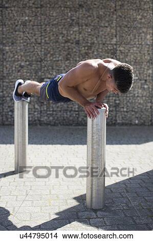 Young man balancing on two bollards, doing push-up. View Large Photo Image Picture - Young man balancing on two bollards, doing push-up.. Fotosearch