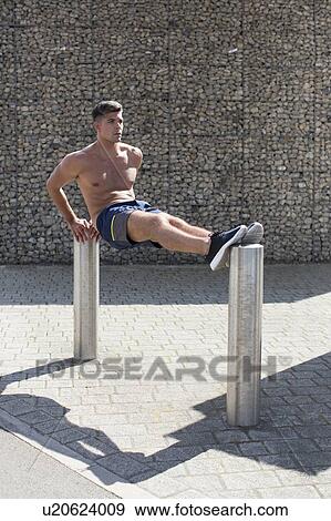 Stock Photo - Young man balancing on two bollards, doing reverse push-up.. Fotosearch
