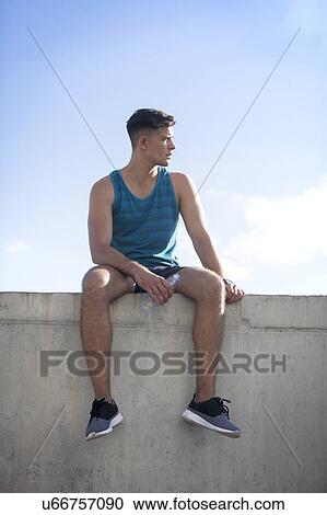 Young man in blue vest sitting on concrete wall, portrait. View Large Photo Image Stock Image - Young man in blue vest sitting on concrete wall, portrait.. Fotosearch