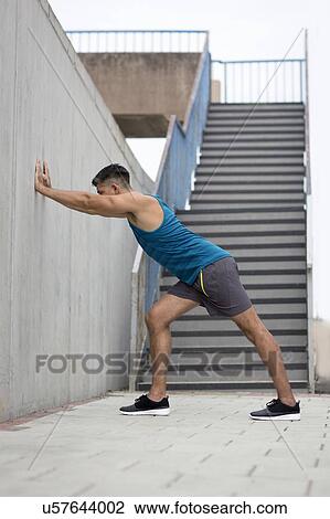 Young man stretching leg against wall. View Large Photo Image Stock Image - Young man stretching leg against wall.. Fotosearch
