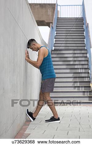 Stock Photo - Young man stretching leg against wall.. Fotosearch