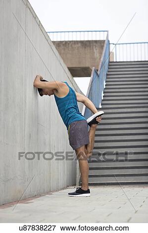 Young man stretching leg by wall. View Large Photo Image Stock Photo - Young man stretching leg by wall.. Fotosearch