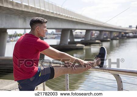 Stock Image - Young man stretching leg on railing before a run.. Fotosearch