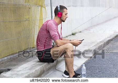 Stock Image - Young man wearing headphones listening to music on Smartphone.. Fotosearch