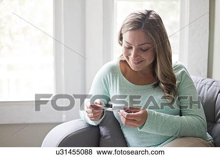 Young woman sitting on sofa and looking at pregnancy test. View Large Photo Image Stock Photo - Young woman sitting on sofa and looking at pregnancy test.. Fotosearch