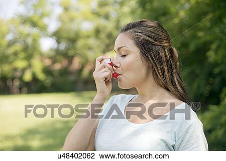 Stock Image - Young woman using an inhaler.. Fotosearch