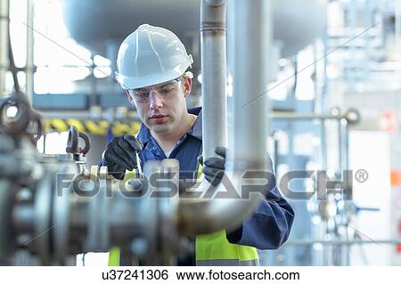 Stock Photograph - Apprentice engineer working on pipeline in industrial product facility. Fotosearch