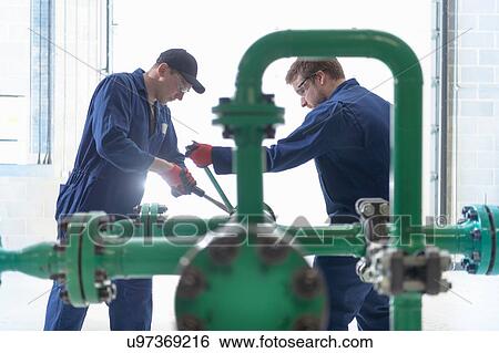Stock Photograph - Apprentice engineers working on pipeline in industrial product facility. Fotosearch