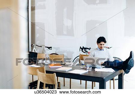 Stock Image - Architect reading with legs propped up on table. Fotosearch