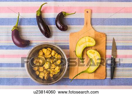 Stock Image - Aubergines, with sliced aubergine on chopping board and pan with prepared food. Fotosearch