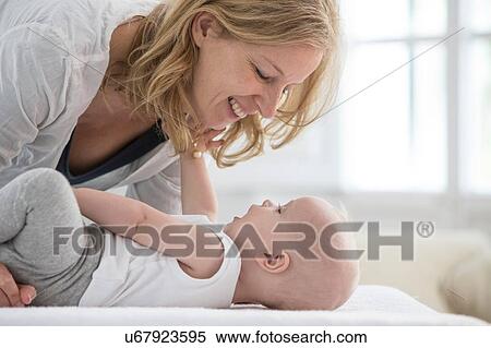 Stock Photography - Baby boy lying on bed face to face with mother. Fotosearch