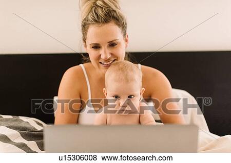 Baby girl and mother sitting up in bed staring at laptop View Large Photo Image Stock Photo - Baby girl and mother sitting up in bed staring at laptop. Fotosearch