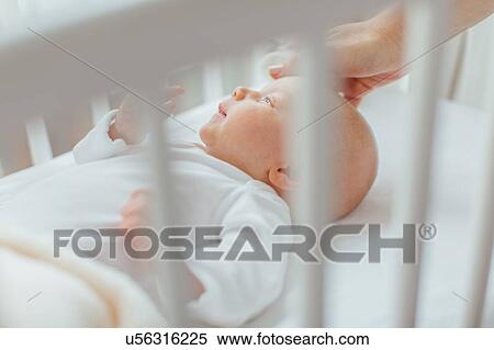 Stock Photography - Baby girl lying in crib, mother's hand soothing head. Fotosearch