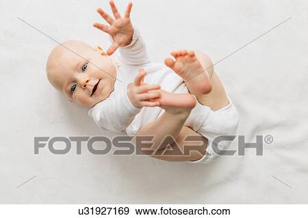 Stock Photo - Baby girl lying on back, arm and legs raised, looking at camera smiling. Fotosearch
